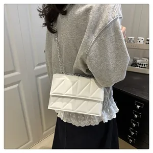Close-up of a white quilted crossbody bag featuring silver chain and geometric stitching