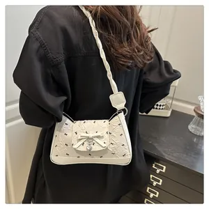 Detail of white textured shoulder bag with black bows and heart pendant on braided strap