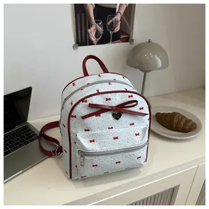 Detail of white mini backpack with red bow prints and a heart-shaped metal pendant charm