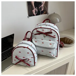 Detail view of two white backpacks with red bow patterns and silver heart charms in a room