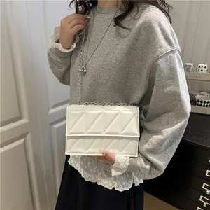 Quilted white crossbody square bag with silver chain strap worn over a grey hoodie