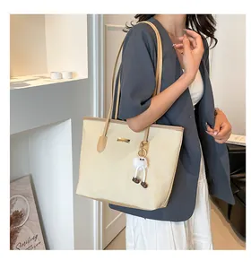 Detail of cream woven tote bag with brown leather handles and cute plush charm pendant