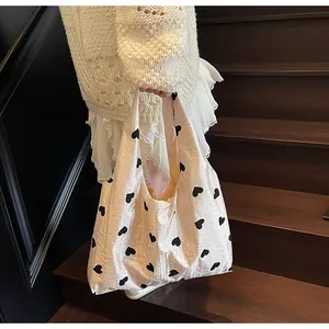 Detail of beige canvas tote bag with black heart patterns held by a model on stairs