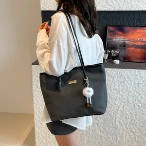 Chic black tote bag with woven texture, golden detail and plush charm on a model