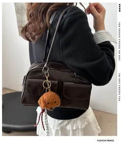Détail d'un sac bandoulière rétro marron avec doubles poches et pendentif ours