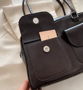 Detalle de bolso en cuero PU marrón oscuro con dos bolsillos de solapa magnética y herrajes plateados