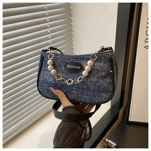 Detail einer blauen Denim-Handtasche mit einer Kette aus Perlen und Silberblumen
