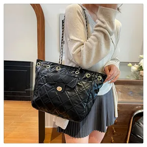 Detail of black quilted tote bag with gold swivel lock and metal chain strap details