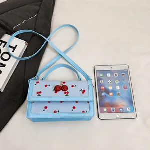 Detalle del bolso azul claro con estampado de cerezas junto a un iPad mini de medida