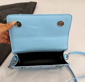 Detalle del bolso bandolera azul que muestra el cierre magnético y el estampado de cerezas
