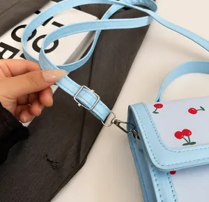 Detalle de la correa ajustable con hebilla plateada en el bolso azul con estampado de cerezas