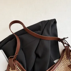 Detail of brown leather handle knotted to a beige woven straw tote bag surface