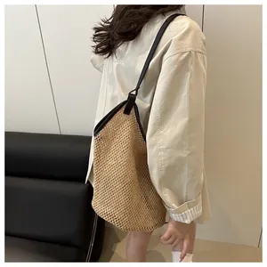 Detalle de bolso tote de paja tejida con correas de cuero negro llevado por una modelo