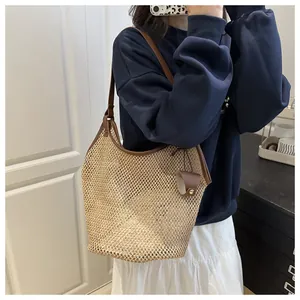 Detalle del bolso tote de paja tejida con ribete de cuero marrón y accesorio colgante