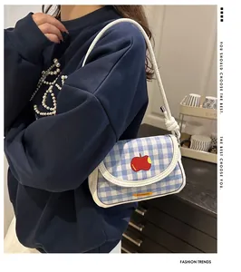 Detail of blue gingham mini shoulder bag featuring a red apple embroidery and knotted strap