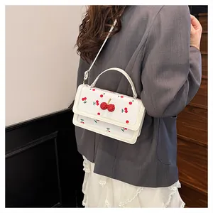 Detalle de bolso bandolera blanco con motivos de cerezas y adorno de cereza en relieve