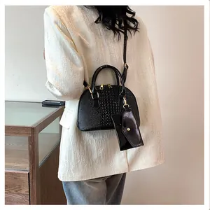 Detail of a black crocodile-pattern shell bag with mini pouch worn as a crossbody