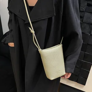 Champagne gold pebbled leather crossbody phone bag with knotted strap on dark coat