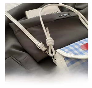 Close-up of adjustable shoulder strap and silver buckle on plaid saddle crossbody bag