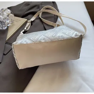 Close-up of ivory dumpling bag with floral embroidery on brown blazer and art books