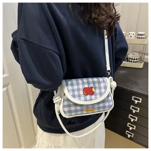 Close-up of blue and white plaid crossbody bag with red apple embroidery and knotted strap