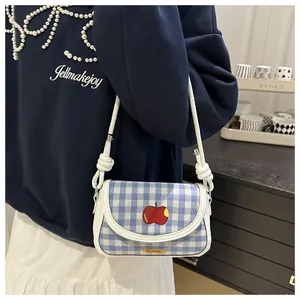Close-up of blue plaid saddle bag with red apple embroidery and knotted strap details