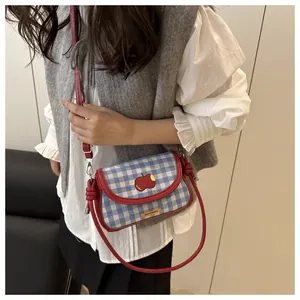 Detail showing red apple patch on blue gingham mini shoulder bag with cross-body strap