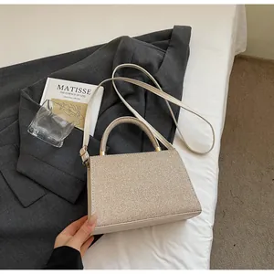 Détail d'un sac à main beige pailleté avec poignée ronde et bandoulière sur un drap blanc chic