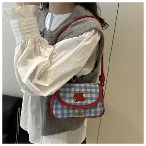 Close-up of a blue plaid canvas crossbody bag with red trim and cute apple embroidery