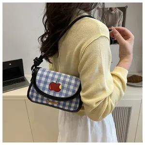 Detail of blue gingham shoulder bag featuring a red apple print and black knotted strap