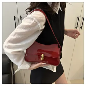 Close-up of a glossy red patent leather underarm bag with an oval gold metal clasp