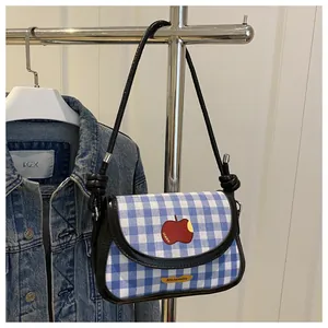 Detail of blue plaid mini shoulder bag with red apple patch and leather strap knots