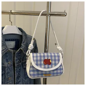 Detail of blue gingham mini shoulder bag featuring a red apple embroidery and knotted strap