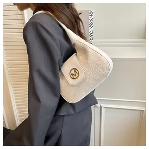 Detail of cream woven underarm bag featuring a metallic gold M logo and stitching