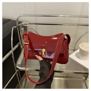 Detail of red patent leather saddle bag with high-gloss finish and gold U-shaped metal lock