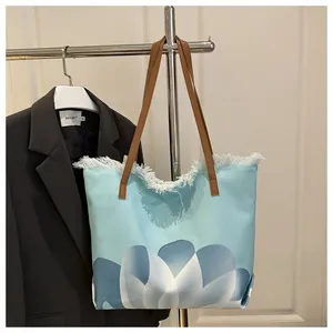 Detalle de bolso tote de lona con flores azules, flecos blancos y correas de cuero