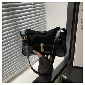 Detail of glossy black patent leather shoulder bag with golden oval turn-lock closure