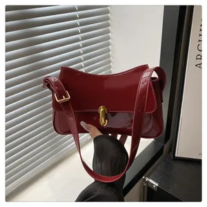 Detail of red glossy leather shoulder bag with gold oval clasp and wavy top design
