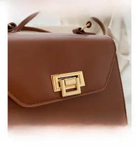 Dettaglio della borsa in pelle marrone con patta diagonale e fibbia rettangolare dorata