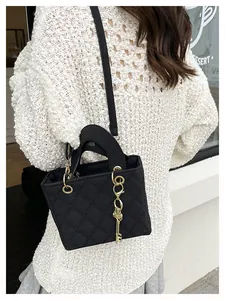 Detailed close-up of a quilted black crossbody bag with gold key charm on a model