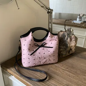 Détail du sac seau en jacquard rose avec nœuds noirs et texture de la poignée en cuir