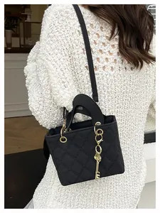Detail of black quilted crossbody bag with a decorative gold key charm on a model