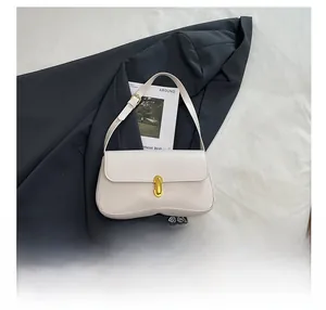 Detail of cream baguette bag showing golden twist lock and size reference with a phone