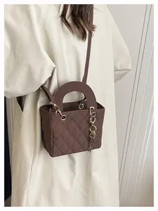 Detail of dark brown quilted square bag with key charm and gold hardware on beige coat