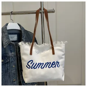 Detalle de bordado Summer y bordes deshilachados en bolso de lona blanca con asas café