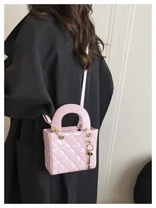 Detail of pink quilted handbag with gold hardware and charm held against black coat