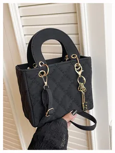 Detail of black quilted shoulder bag with golden key charm and top handle strap