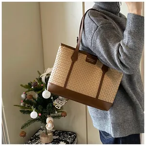 Détail du cabas tressé beige avec garniture en cuir marron porté par un mannequin en studio