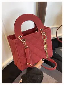 Detail of wine red quilted handbag with circular handle and golden key charm