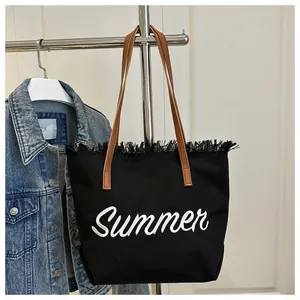 Detalle del bordado Summer y bordes deshilachados en un bolso tote de lona negra